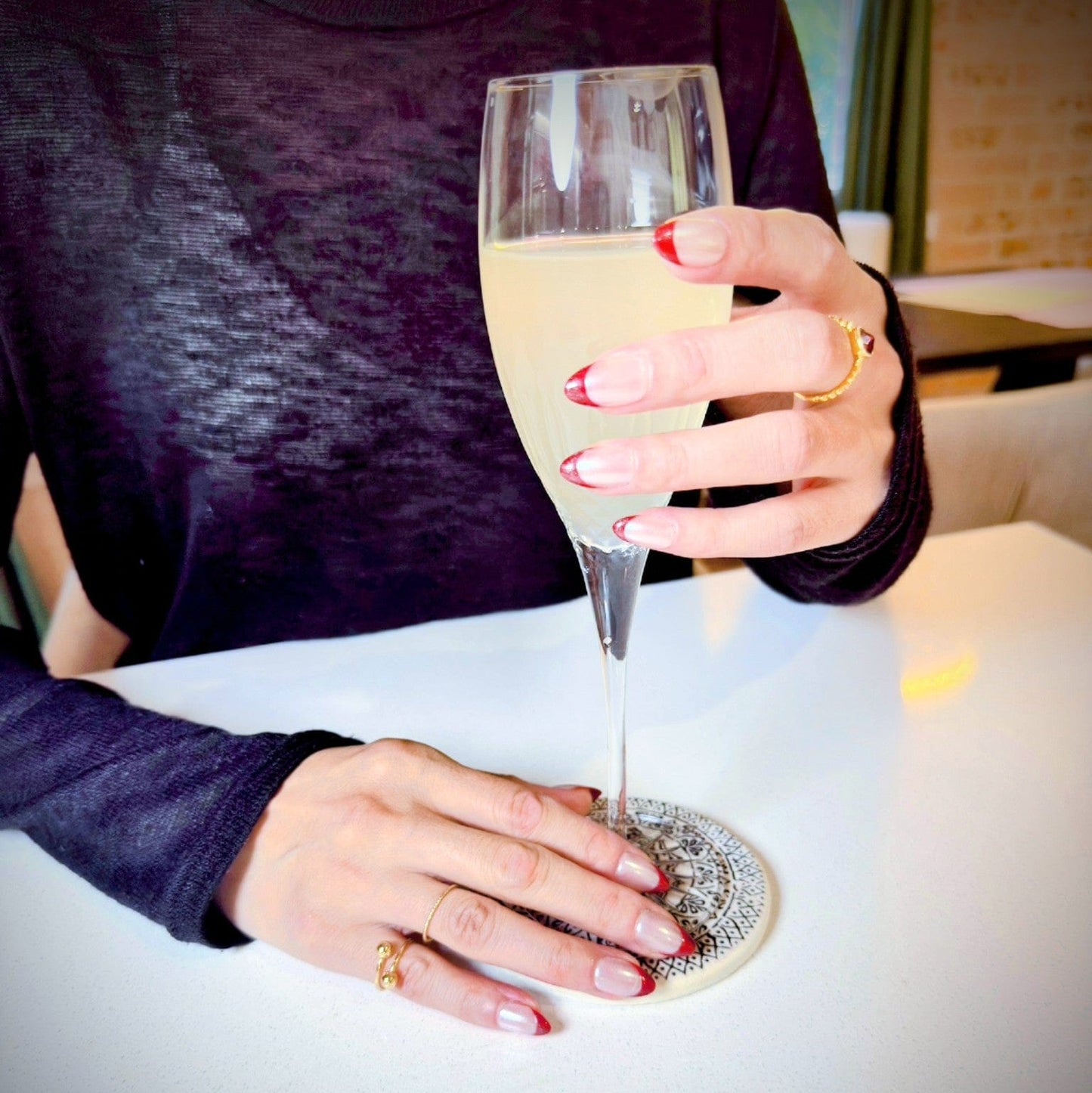 Hands wearing salon quality chrome finish press-on nails, holding a glass of champagne.