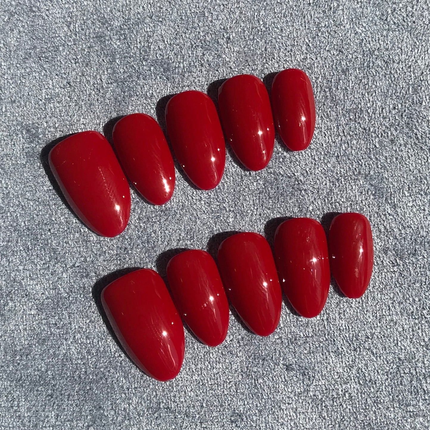 A set of ten glossy red press-on nails arranged in two rows on a textured gray background.