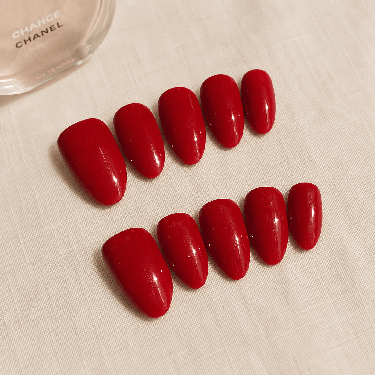 Calm Storm handmade red press-on nails on a light beige surface, with a partial Chanel bottle visible in the top left corner.