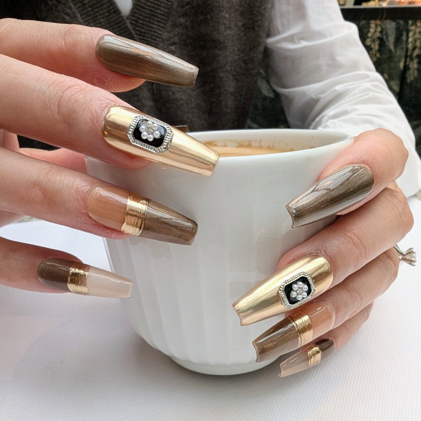 Hands modelling handcrafted designer style press on nails, featuring gold, taupe, chrome strip and rhinestones.