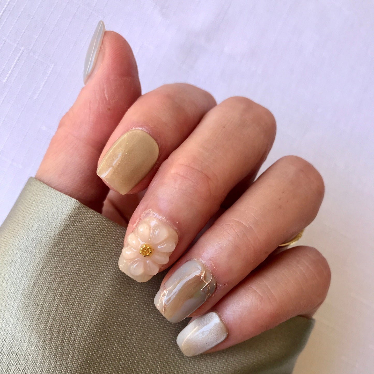 Hand with green and beige press-on nails with a 3d floral design in short square
