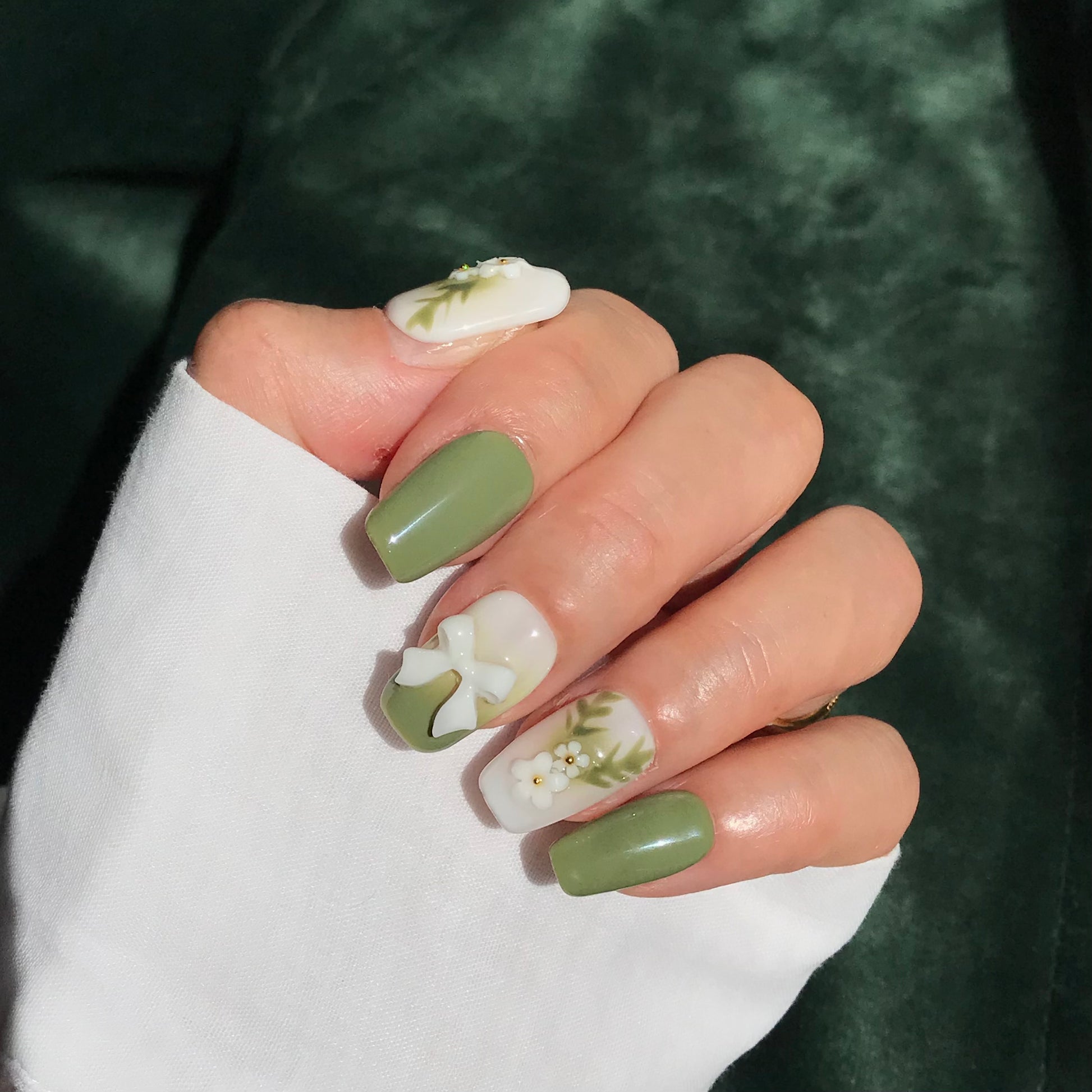 Close-up of a hand with green and white press-on nails with 3D designs in medium square.