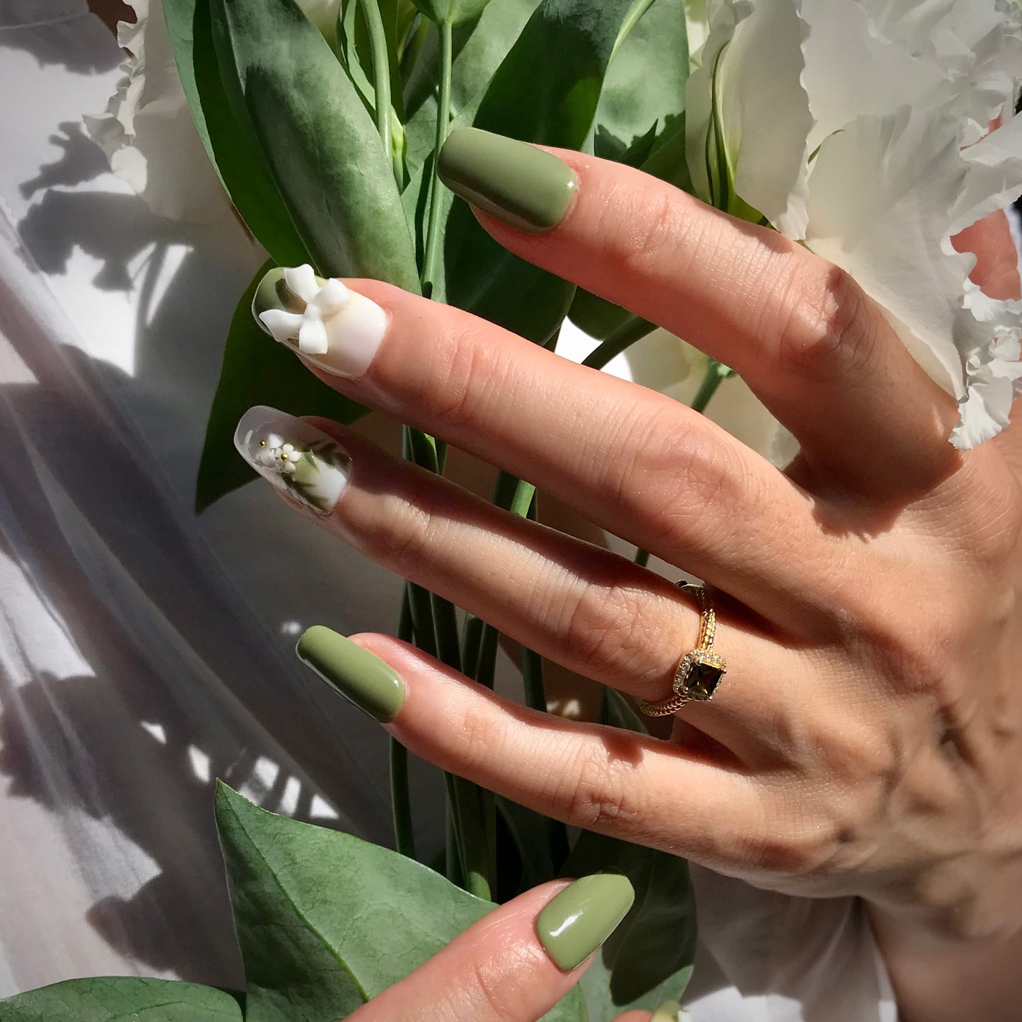 Lifestyle shot of green and white press-on nails with 3D floral designs in medium square.