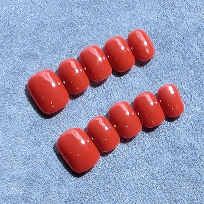Handmade press-on nails in warm brick red in extra short round.