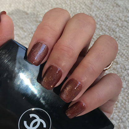 A close-up of a hand wearing press-on nails in shimmery bronze-brown glitter.