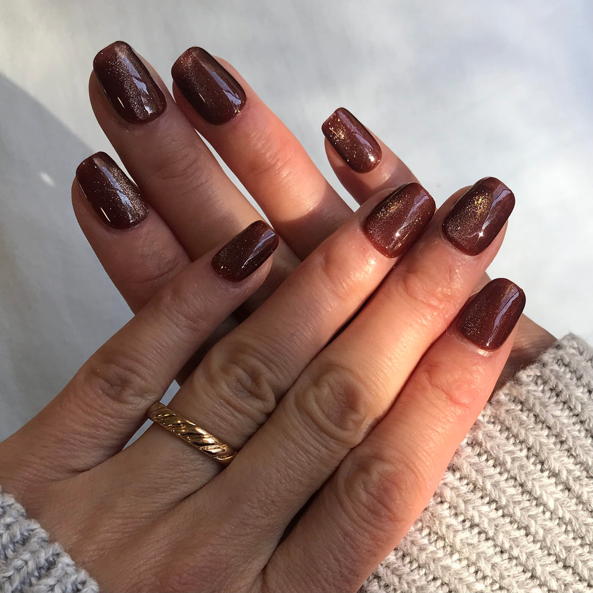 A close-up of a hand with glossy dark brown press-on nails featuring a subtle shimmer.