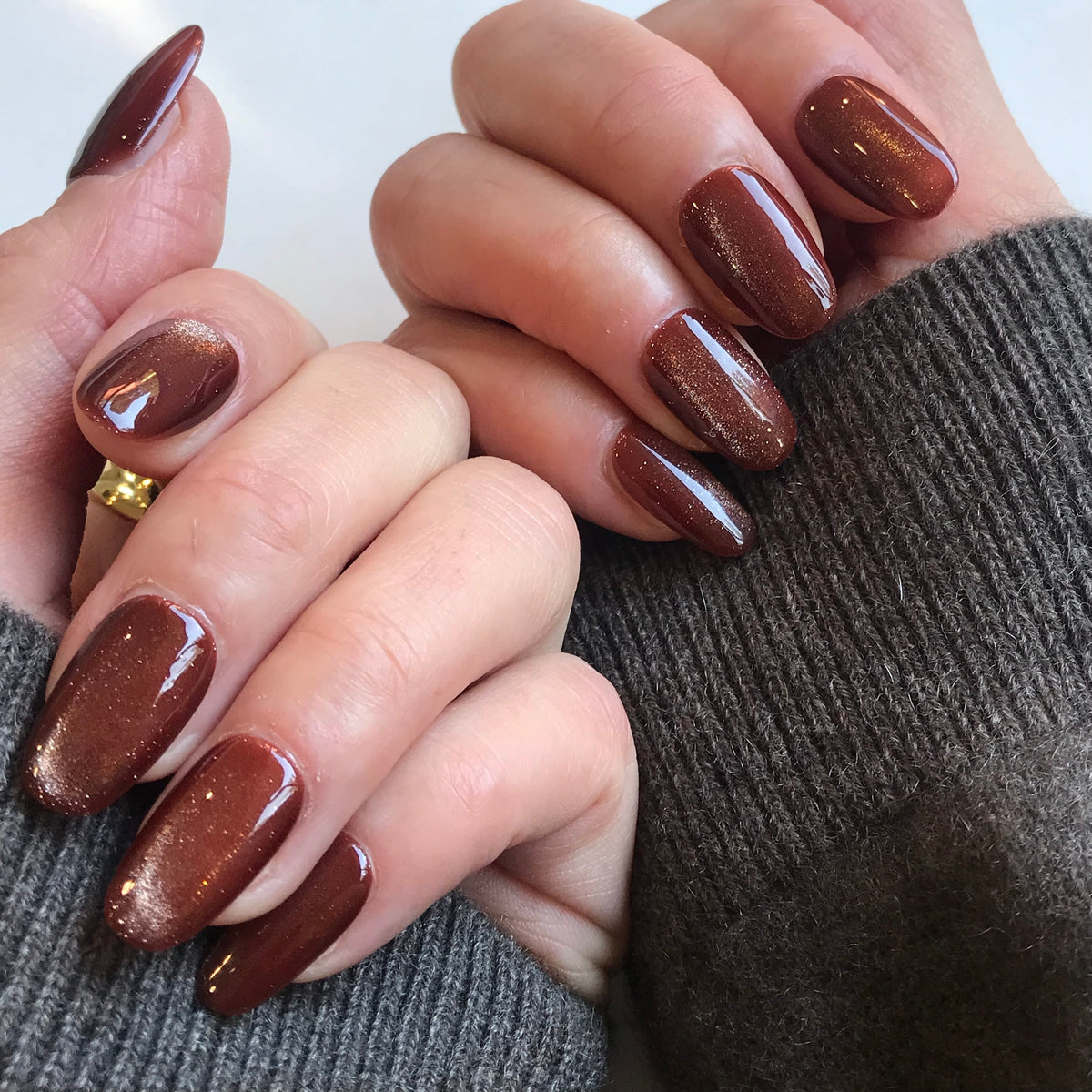 Close-up of hands with glossy brown oval-shaped bronze press-on nails featuring a subtle shimmer.