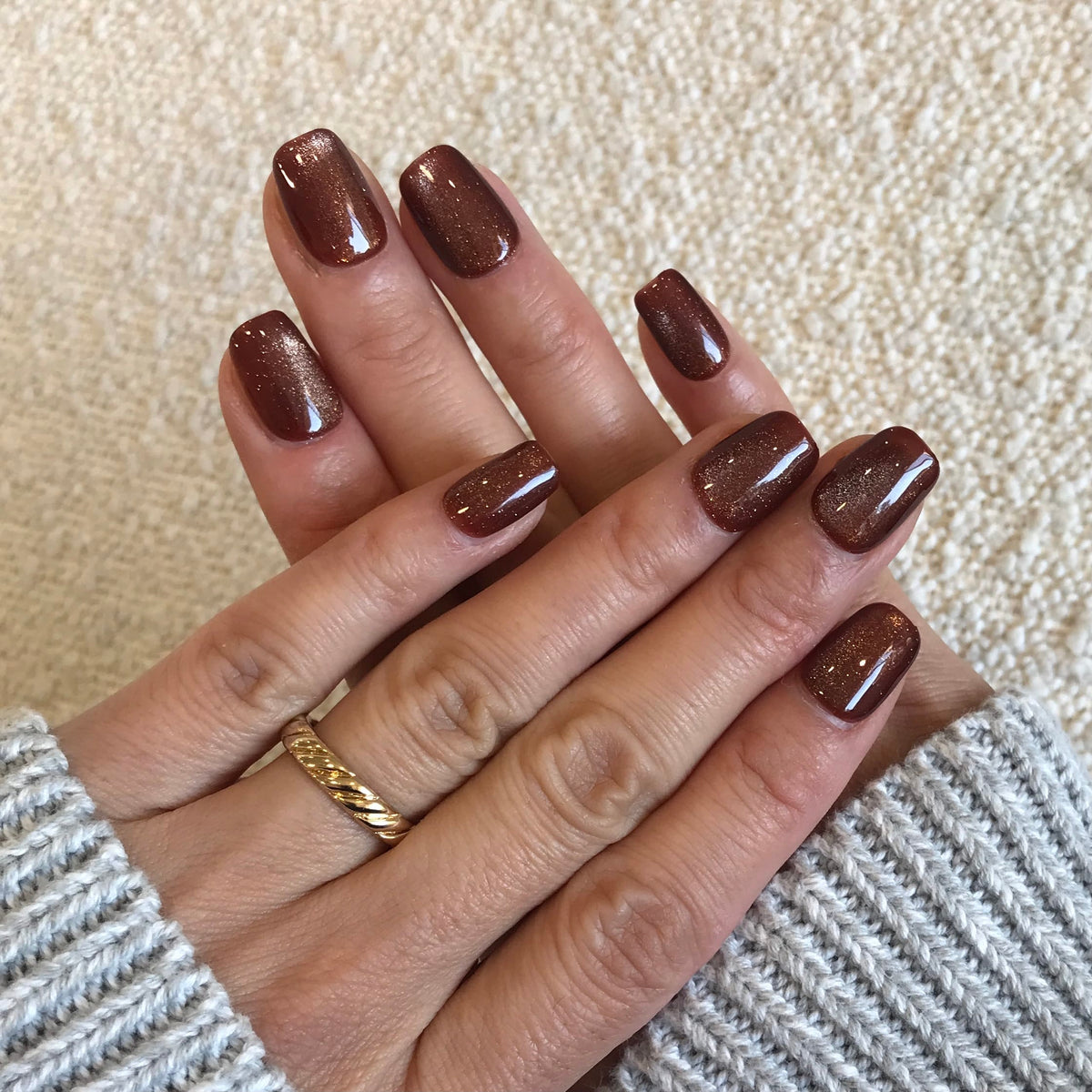 A close-up of hands wearing glossy brown glitter press-on nails.