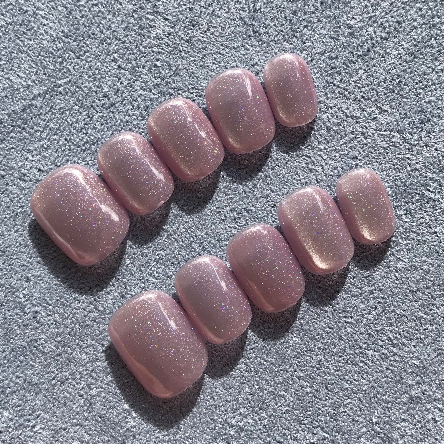 Close up of handmade press-on nails in light lavender with glittering cat eye effect in extra short round shape. 