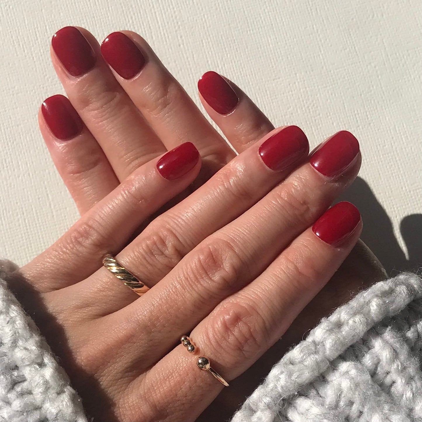 Close-up of hands modelling luxury handmade press-on nails in high gloss classic red. 