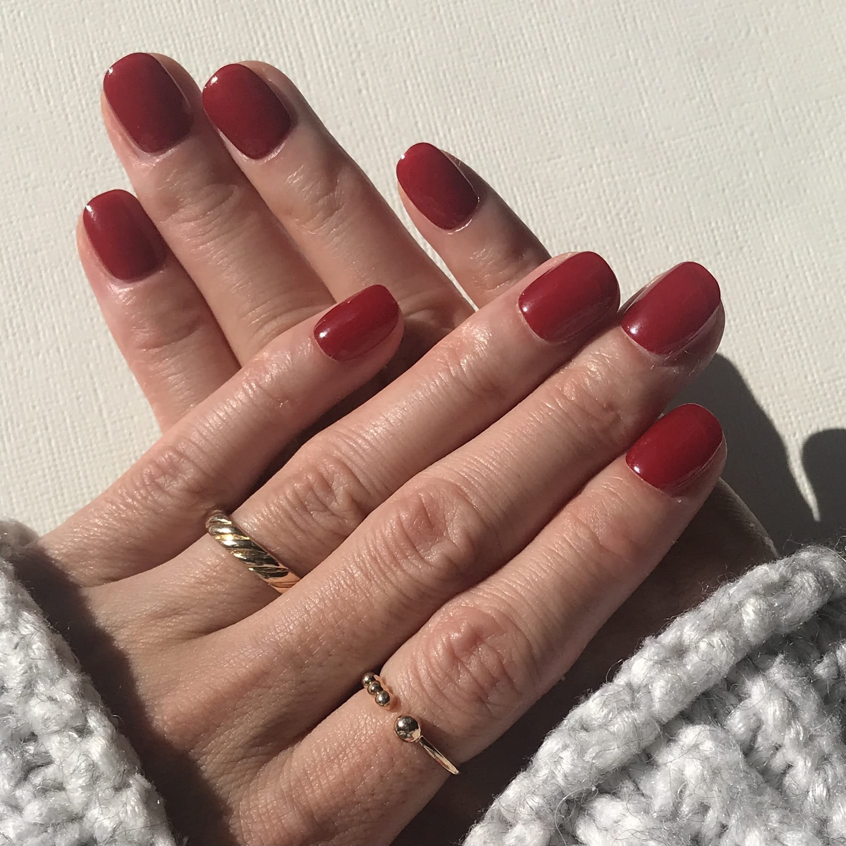 Close-up of hands modelling luxury handmade press-on nails in high gloss classic red. 