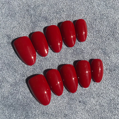 A set of ten glossy red press-on nails arranged in two rows on a textured gray background.