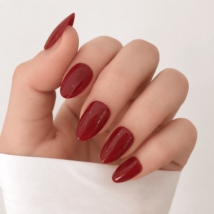 A close-up of a hand with long, almond-shaped press-on nails in a glossy deep red.