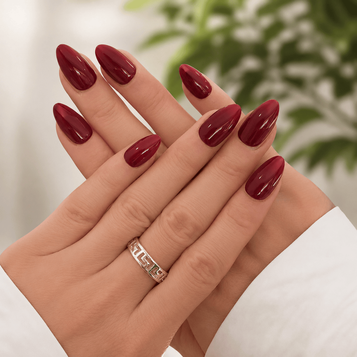 A close-up of hands with glossy, almond-shaped press on nails in classic red.