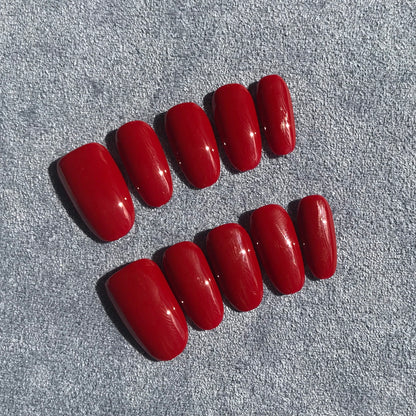 Ten red press-on nails with a glossy finish, on a textured gray background.