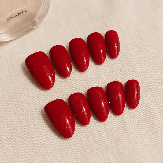 Calm Storm handmade red press-on nails on a light beige surface, with a partial Chanel bottle visible in the top left corner.