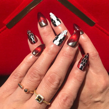Hands wearing luxury designer press-on nails featuring serpentine texture in red, gold, black and white. 