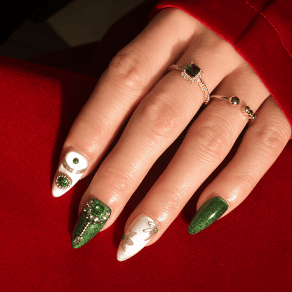 A close up of a hand wearing luxury press-on nails in emerald green featuring silver beads and floral design.