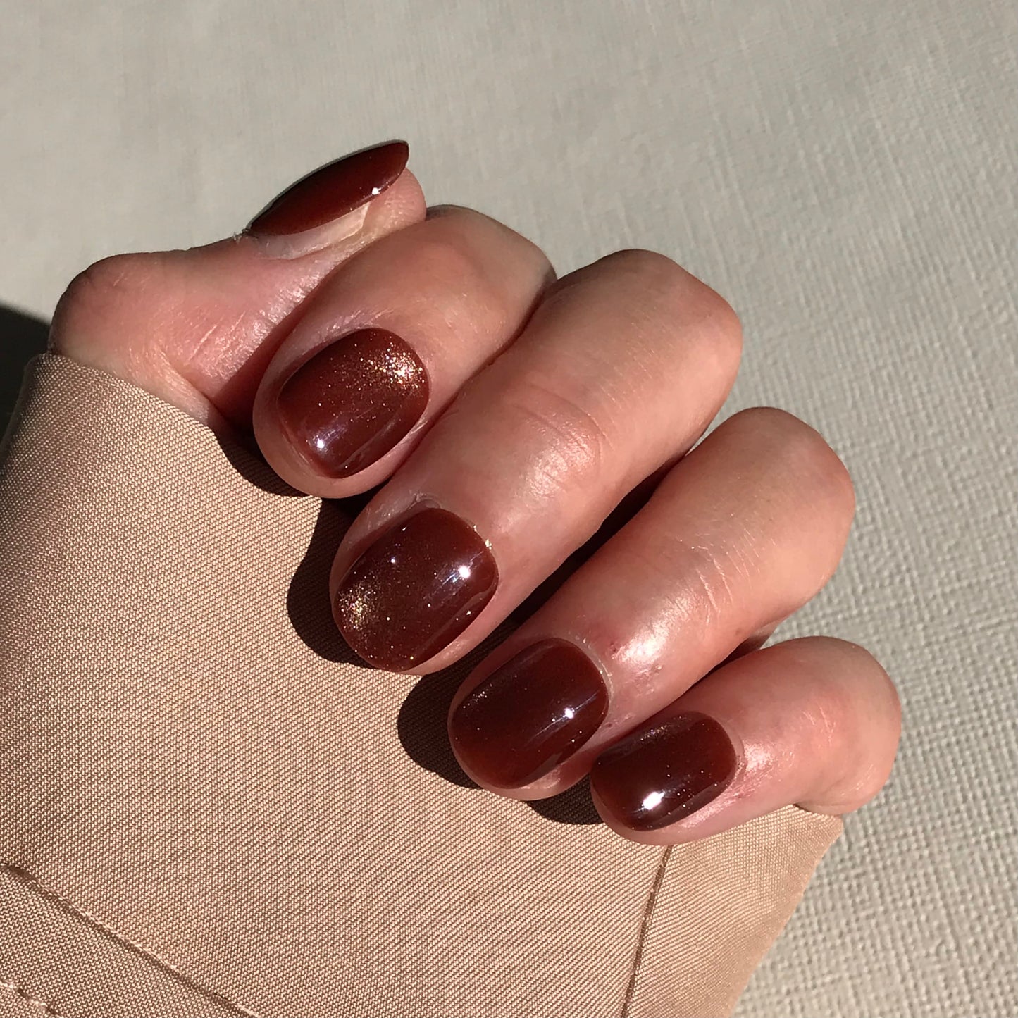 Hand with brown glitter press-on nails on a neutral background.