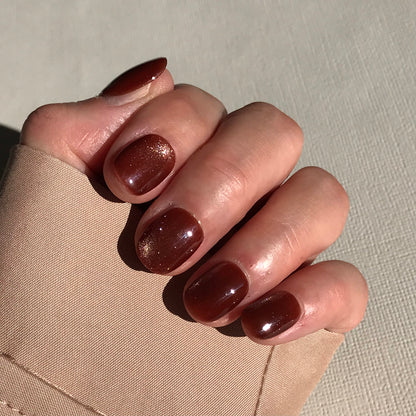 Hand with brown glitter press-on nails on a neutral background.