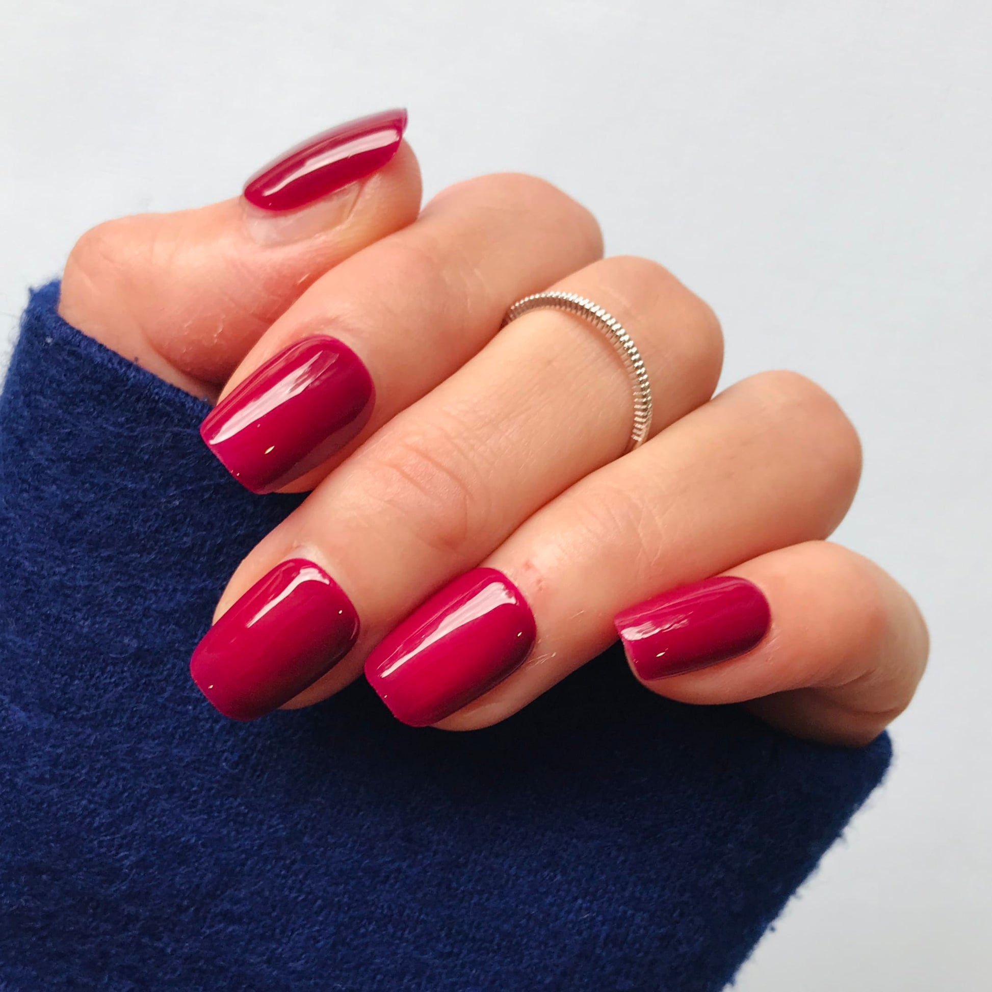 Close up of a hand wearing luxury high gloss press-on nails in fuchsia. 