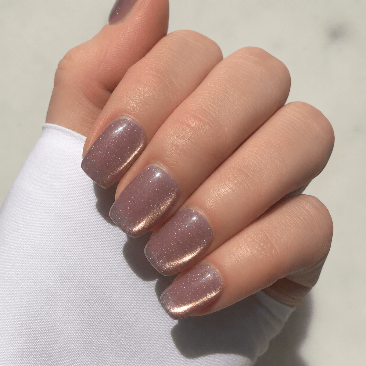 A hand modelling mauve coloured press-on nails with cat eye shimmer. 