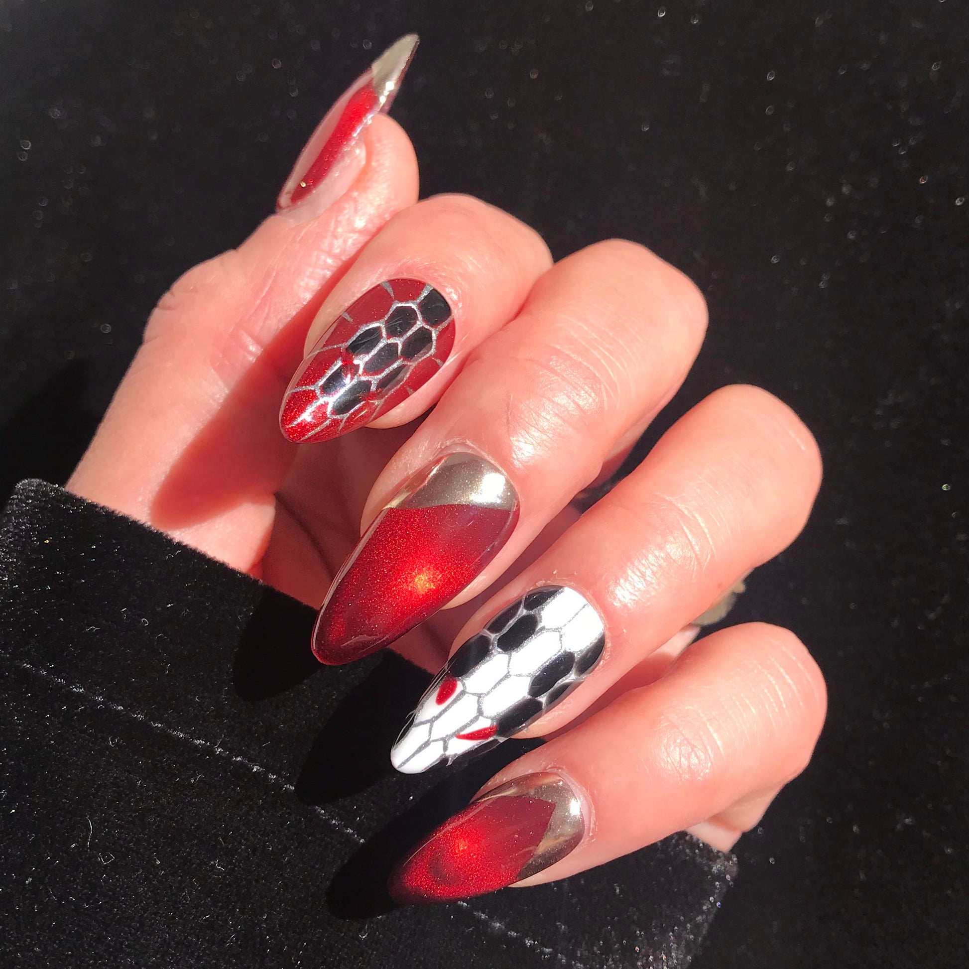 A close up of a hand wearing almond shaped press-on nails featuring snakeskin design in ruby red and gold.