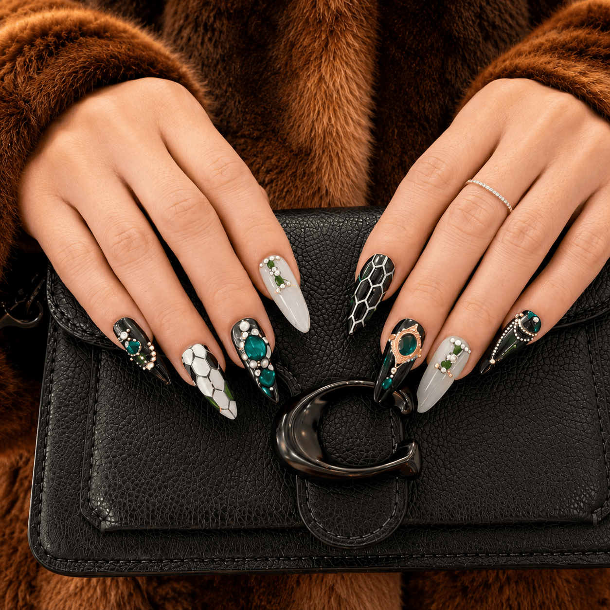 A close-up of handcrafted press-on nails decorated in green, black, white, and gold patterns with gem stones and silver beads. 