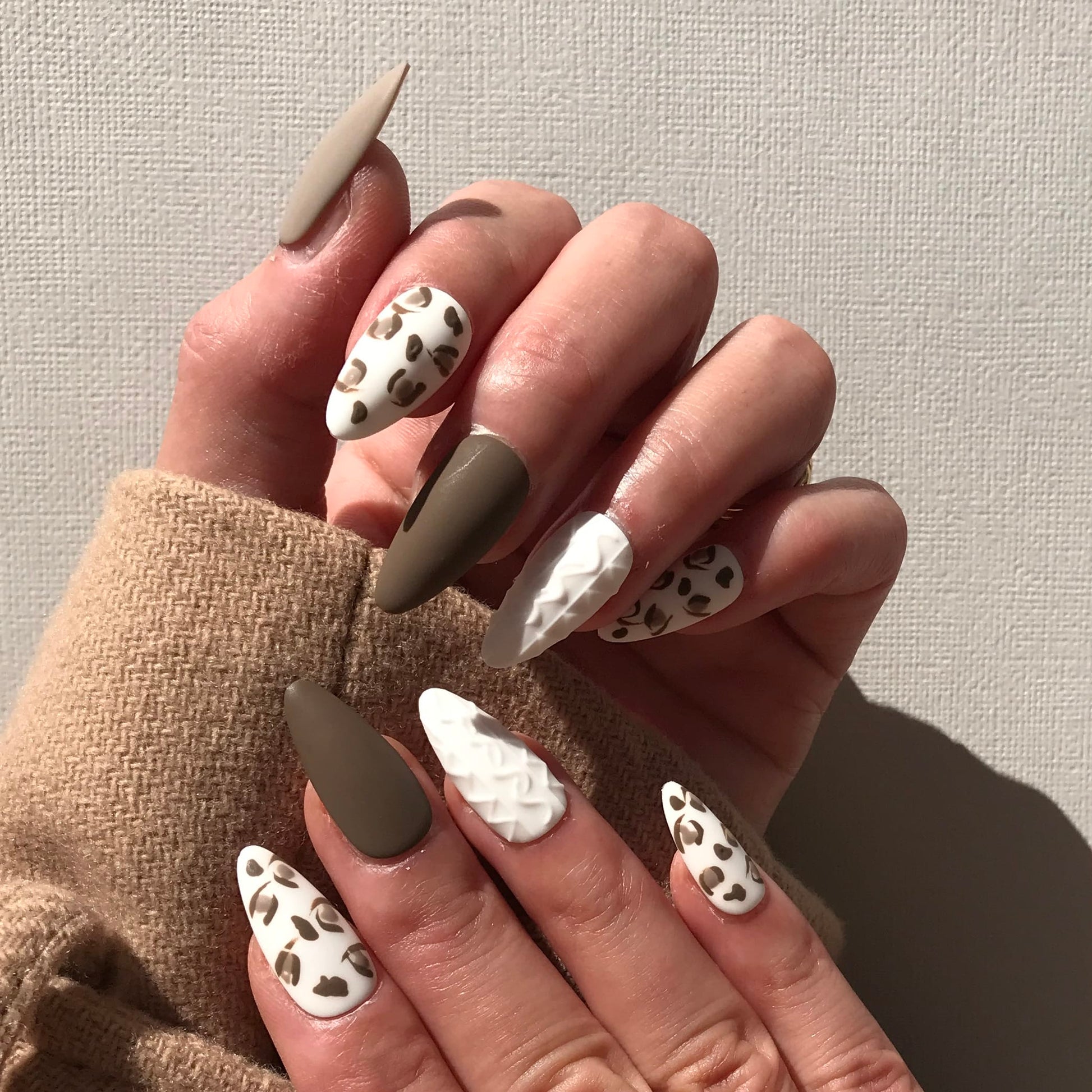 Hand with almond-shaped press-on nails featuring a neutral color palette and animal print design.