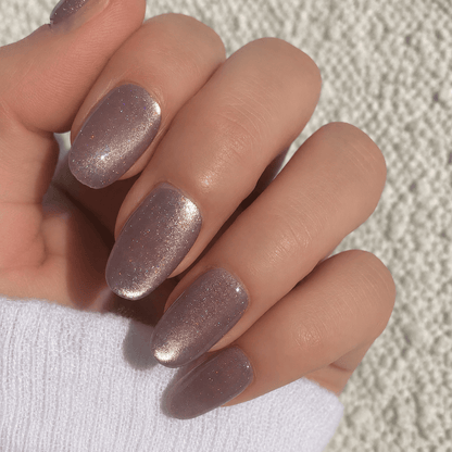 A close-up of a hand with press-on nails in a shimmering metallic mauve-pink.