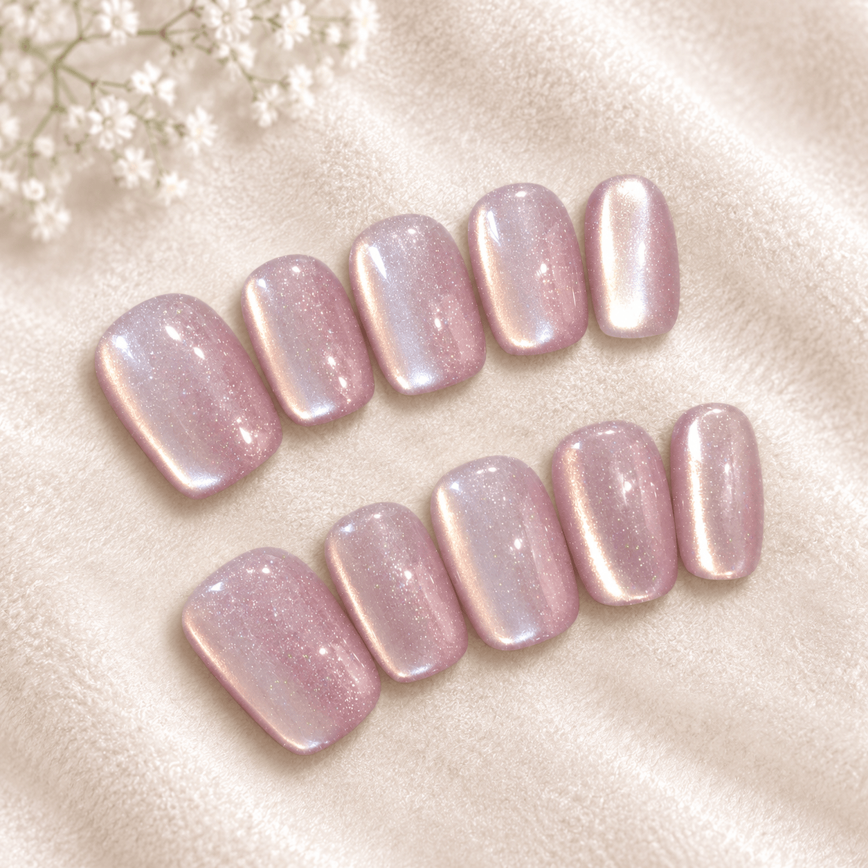 Ten press-on nails with a soft pink and iridescent shimmer, arranged on a beige  background