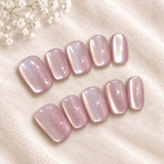 Ten press-on nails with a soft pink and iridescent shimmer, arranged on a beige  background