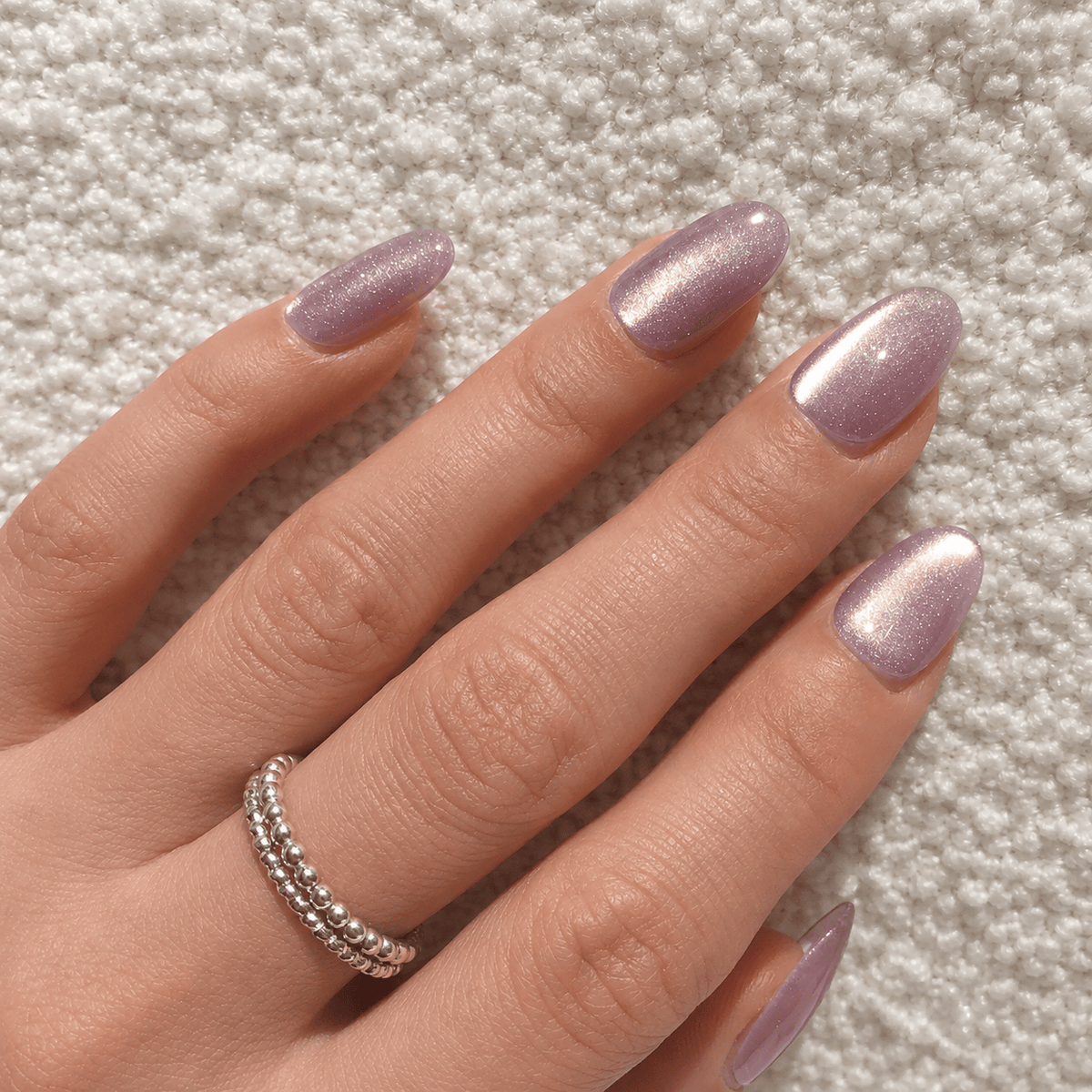 A close-up of a hand with press-on nails in shimmering metallic lavender-purple colour.