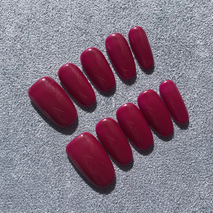 A set of ten press-on nails in a glossy deep magenta color, arranged on a textured gray fabric background.