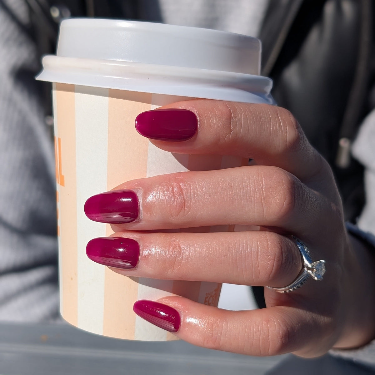 A close-up of a hand with glossy deep magenta press on nails in oval shape. 