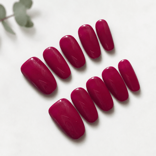 A set of glossy magenta-pink press-on nails arranged on a white background.