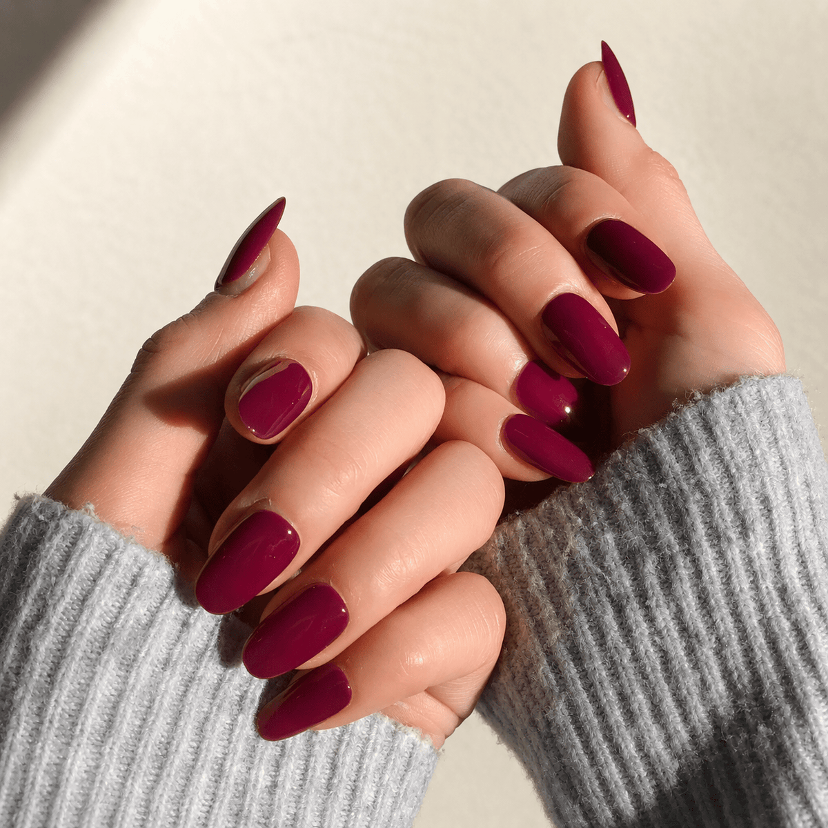 A close-up of long, almond-shaped press on nails in a deep berry purple colour. 