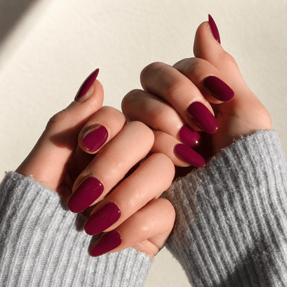 A close-up of long, almond-shaped press on nails in a deep berry purple colour. 