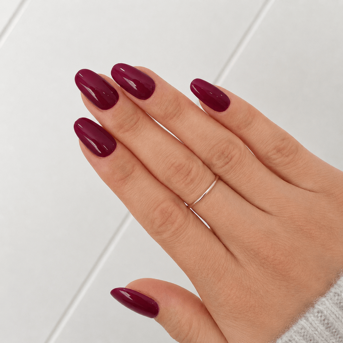 A close-up of a hand wearing glossy deep burgundy press on nails in oval shape.