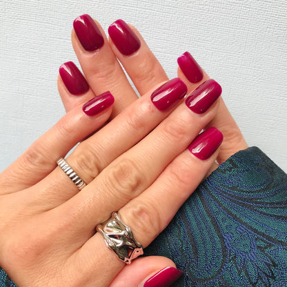 Close-up of hands wearing vibrant fuchsia press-on nails in short square. 