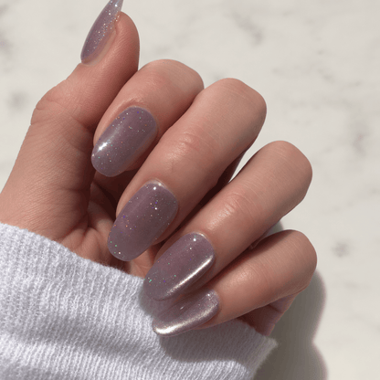 A close-up of a hand with press-on nails in a shimmering lavender glitter.