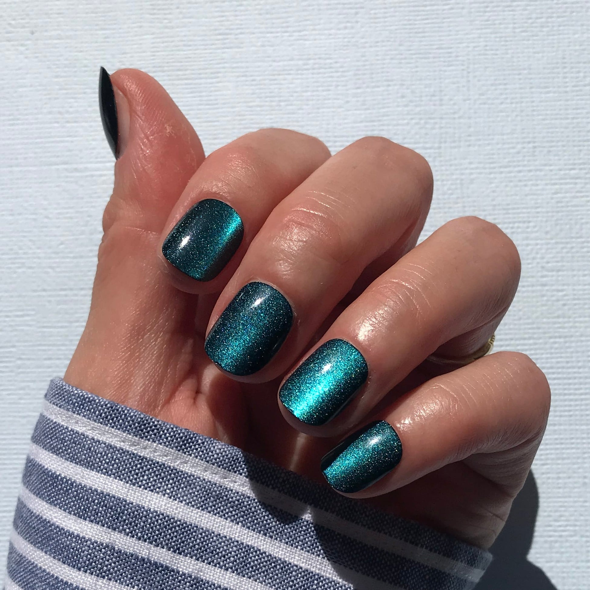 Close up of handmade press-on nails in peacock green with cat eye effect in extra short. 
