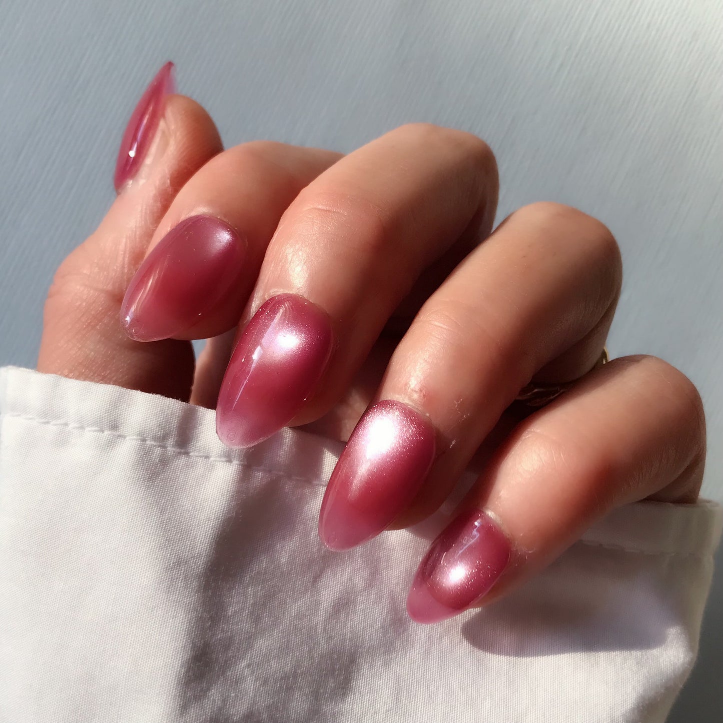 Close-up of a hand with pink press-on nails in medium almond with cat eye design.  