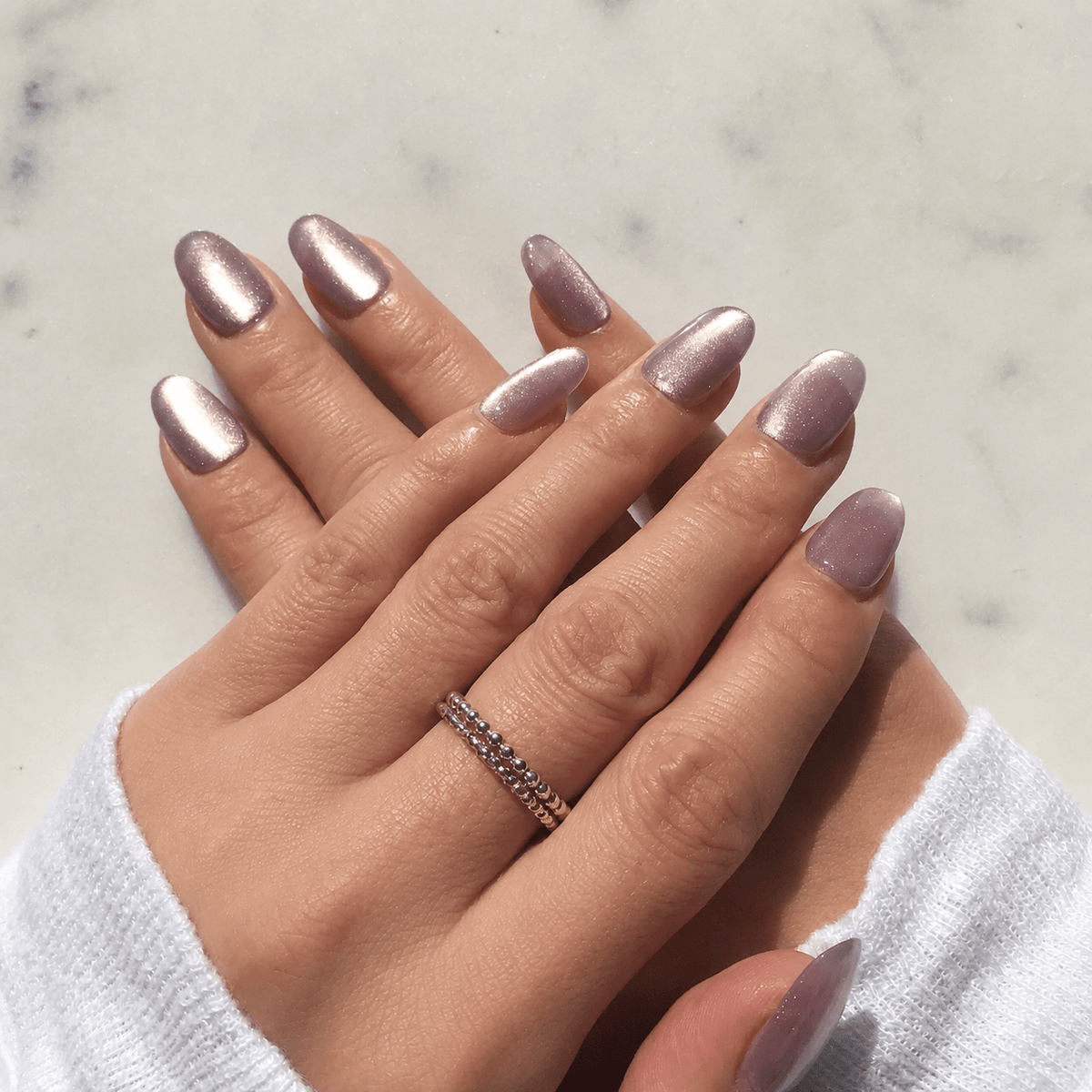 A close-up of a hand with oval shaped, glossy, metallic mauve-pink press-on nails.