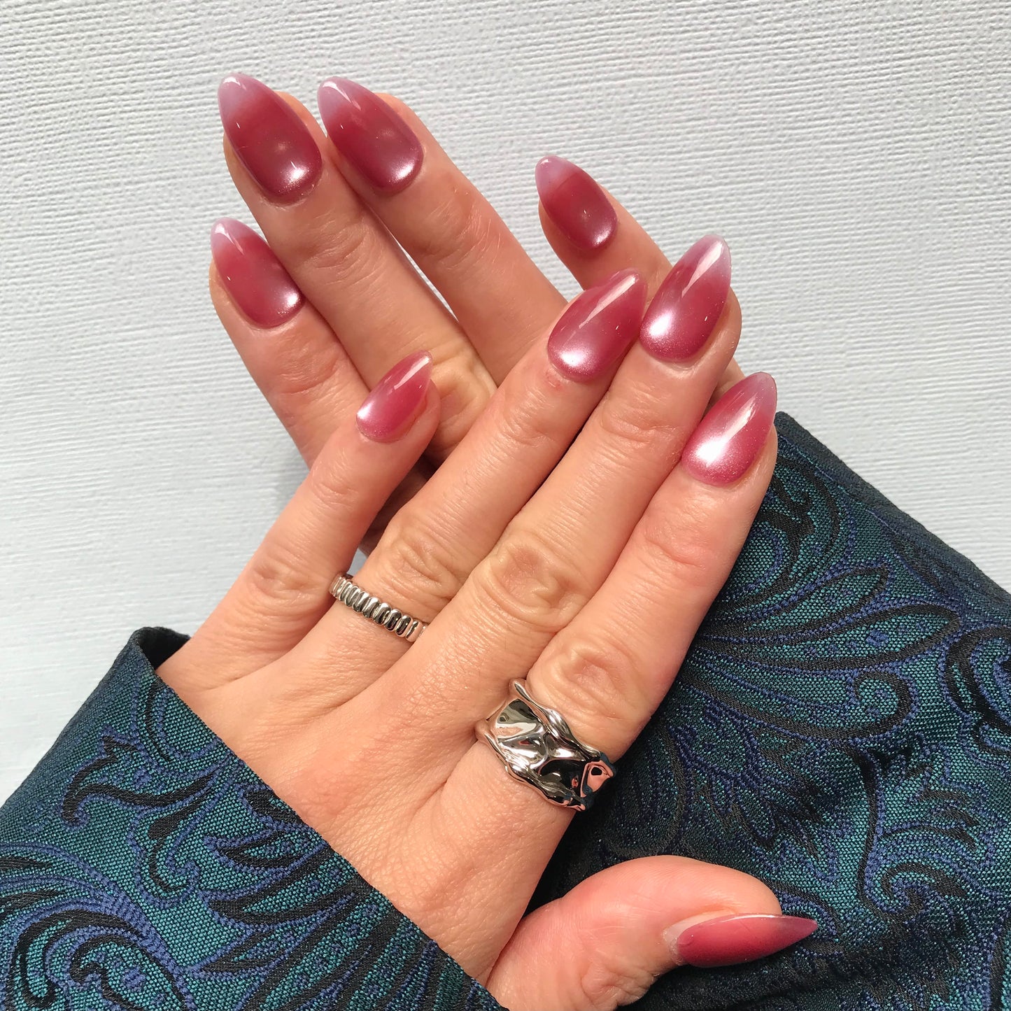 Close-up of hands with pink press-on nails in medium almond shape with a cat eye design. 