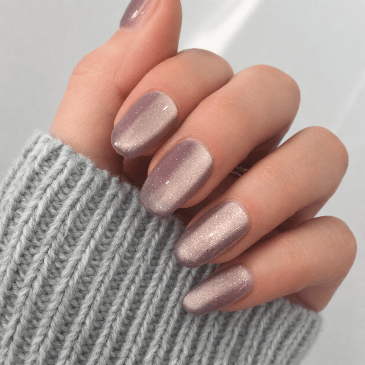 A close-up of a hand with press-on nails in a shimmering dusty mauve-purple shade.