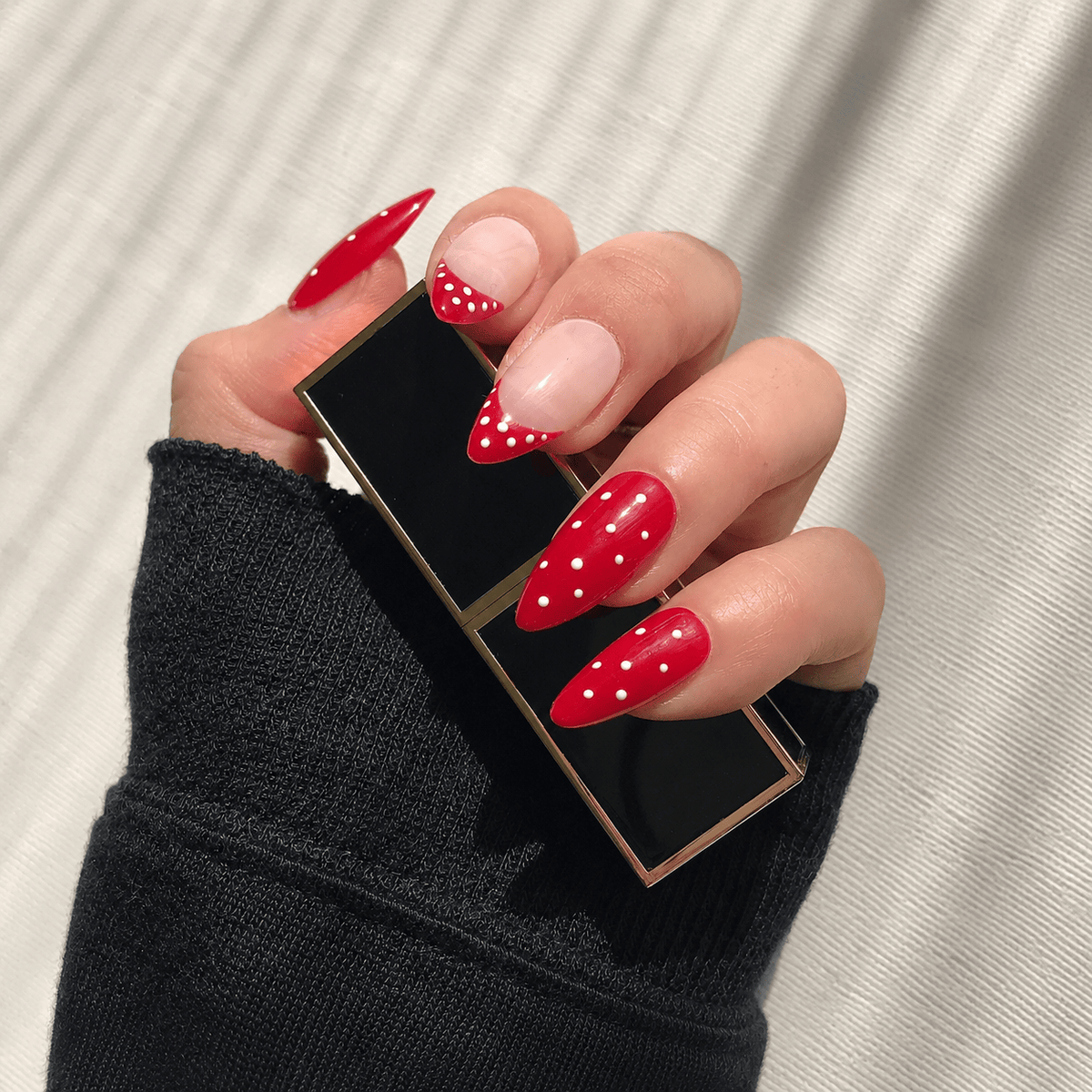 A hand with handmade press-on nails in a red and white polka dot pattern.
