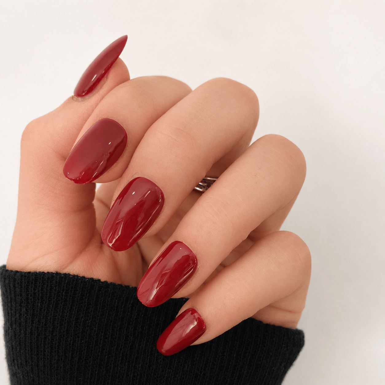 A close-up of a hand with glossy, oval-shaped press-on nails in a glossy deep red.