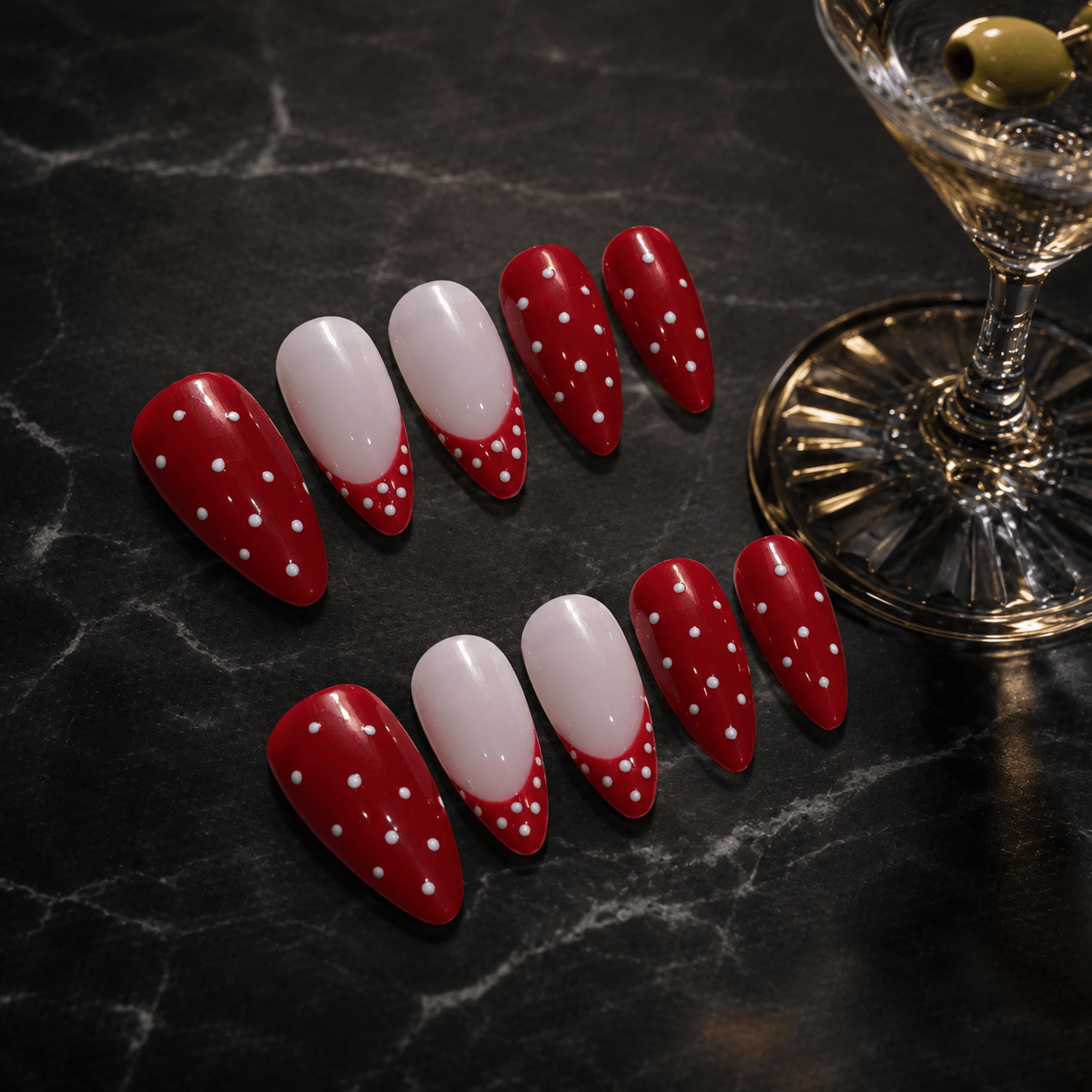 Calm Storm premium red and white polka dot nail art on a dark marble surface with a cocktail glass.