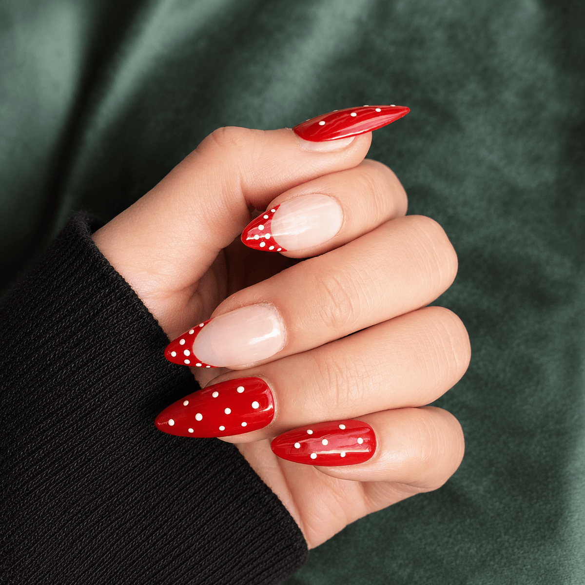 A close-up of a hand with long, glossy red stiletto-style press-on nails with white polka dots.